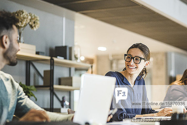 Lächelnde Geschäftsfrau  die einen Mitarbeiter während der Arbeit im Kreativbüro ansieht