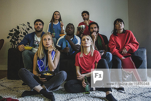 Männliche und weibliche Fans sehen sich zu Hause sitzend ein Fußballspiel an