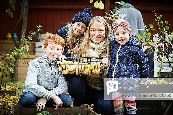 Porträt einer lächelnden Mutter mit kauerndem Kartoffelkorb von Kindern im Hof