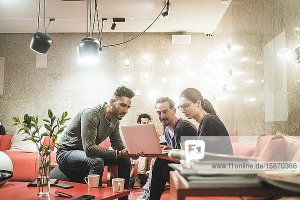 Männliche und weibliche Mitarbeiter  die über einen Laptop arbeiten  während sie im Kreativbüro sitzen