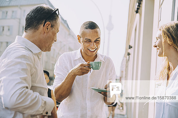 Lächelnder Geschäftsmann trinkt Kaffee mit Kollegen im Straßencafé in der Stadt