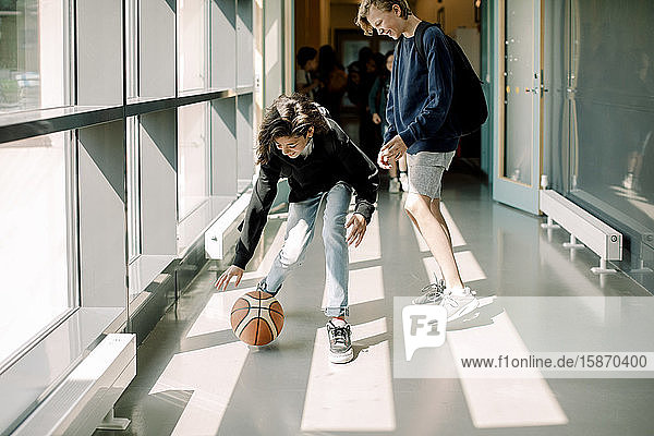 Lächelnde männliche Schüler spielen mit Basketball auf dem Schulkorridor
