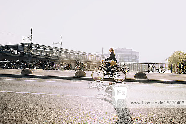 Unternehmerin fährt Fahrrad auf Straße in Stadt gegen Himmel