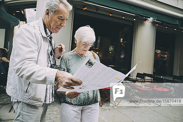 Älteres Ehepaar liest Karte  während es im Urlaub in der Stadt auf dem Bürgersteig steht