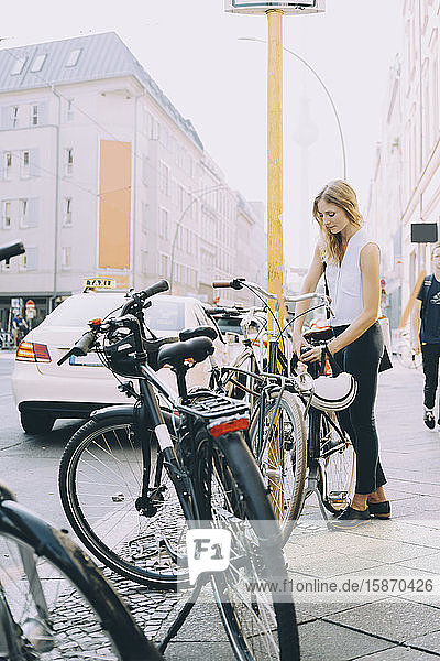 Jungunternehmer schließt Fahrrad in voller Länge auf dem Bürgersteig in der Stadt ein
