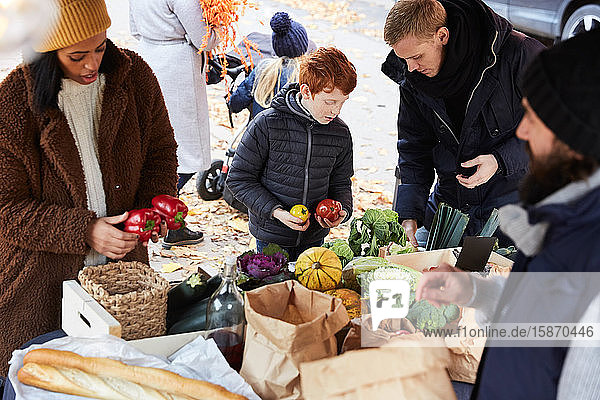 Familie kauft frische Paprikaglocken von männlichem Verkäufer am Marktstand