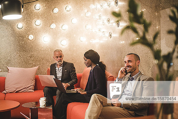 Male entrepreneur talking on mobile phone while sitting with colleagues in office