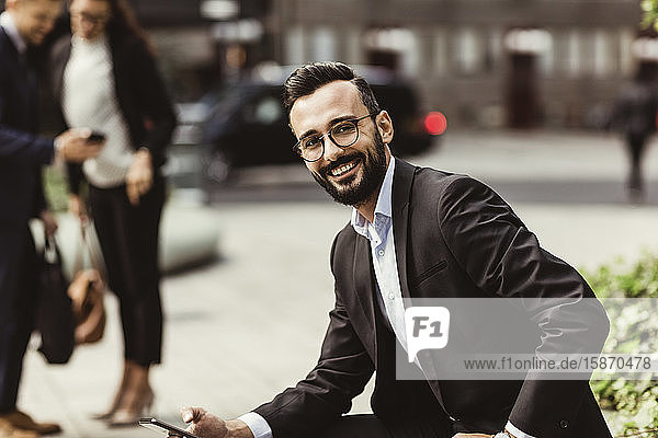 Portrait of smiling businessman with mobile phone sitting outdoors