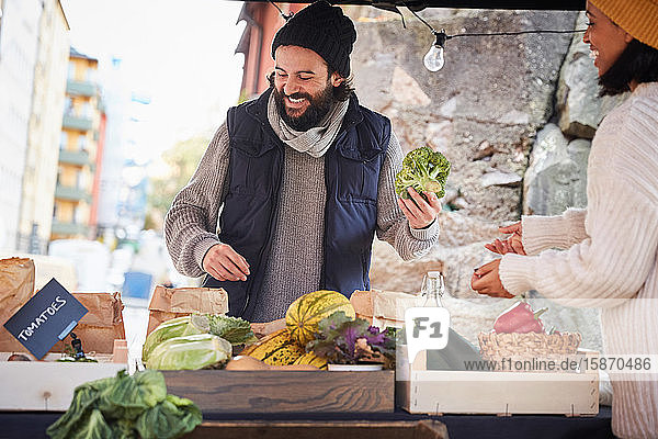 Lächelnder Mann kauft frischen Brokkoli von weiblichem Marktverkäufer am Gemüsestand