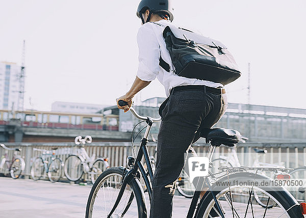 Rear view of businessman with backpack riding bicycle on sidewalk in city