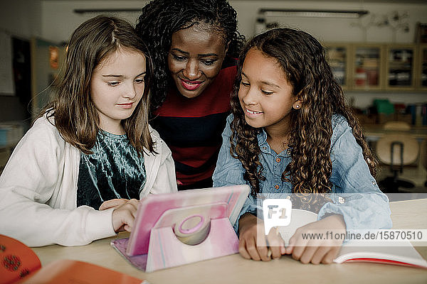 Tutorin mit Schülerinnen  die sich im Klassenzimmer ein digitales Tablet ansehen