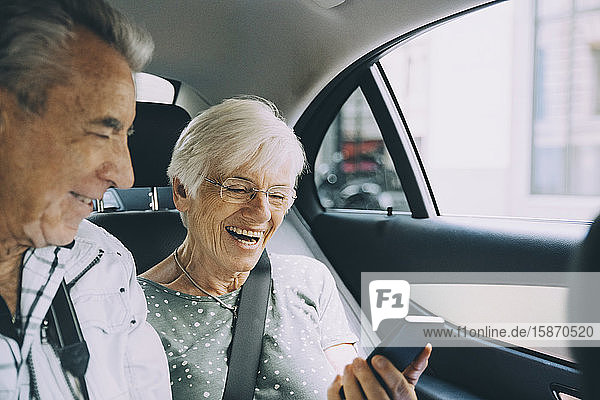 Smiling retired couple using mobile phone while sitting in car during vacation