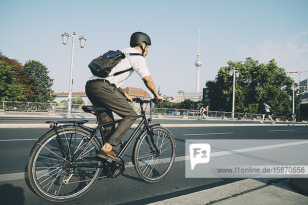 Geschäftsmann mit Helm fährt Fahrrad auf Straße in Stadt gegen Himmel