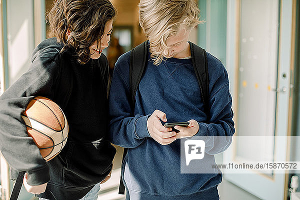 Männliche Schüler mit Smartphone auf dem Schulflur