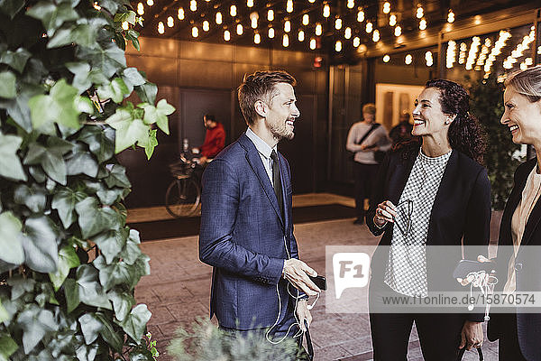 Männlicher Unternehmer lächelt mit seinen Mitarbeitern  während er am Gebäudeeingang steht