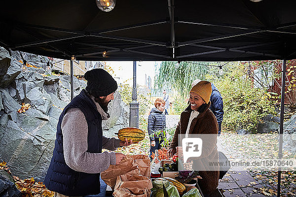 Lächelnde Frau kauft am Gemüsestand frischen Kürbis von männlichem Marktverkäufer