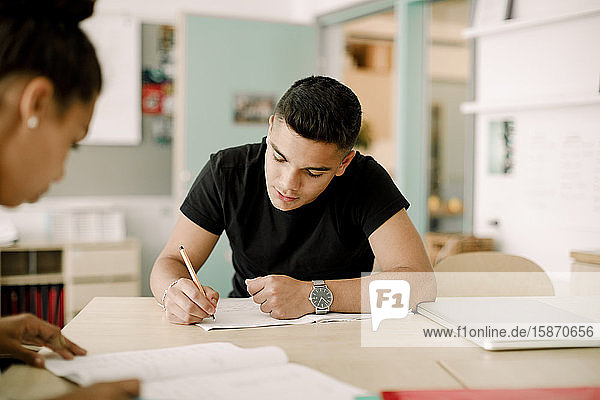 Männlicher Teenager schreibt  während er im Klassenzimmer sitzt