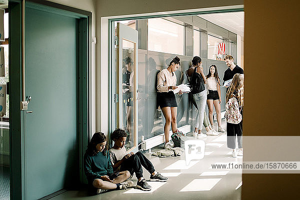 Girl and boy sitting in doorway while professor talking to students in school corridor