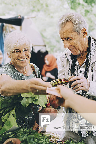 Ältere Frau bezahlt einen Verkäufer  während sie auf dem Markt in der Stadt Gemüse einkauft