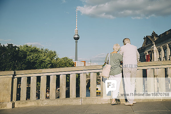 Rückansicht eines älteren Paares  das an einem sonnigen Tag von der Brücke in der Stadt auf den Kommunikationsturm schaut