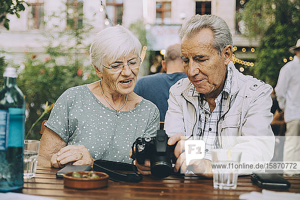 Senior man showing camera to woman while sitting at restaurant in city