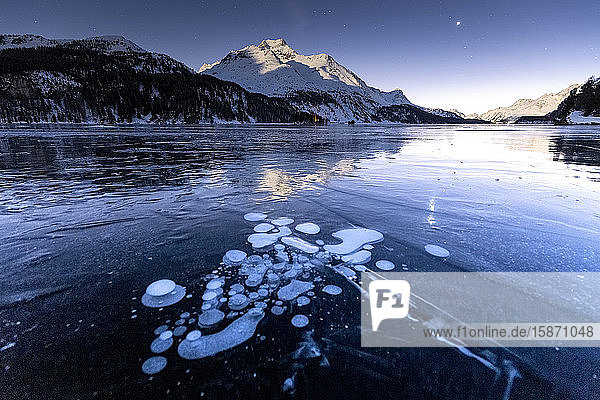 Methane bubbles in the icy surface of the lake with snowy peak illuminated by moonlight Sils Engadine Valley Graubunden Swiss Alps Switzerland Europe