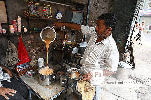 Ein geschäftiger Chaiwallah schenkt Tee an einem Chai-Stand in den Gassen der Altstadt von Ahmedabad  Gujarat  Indien  Asien