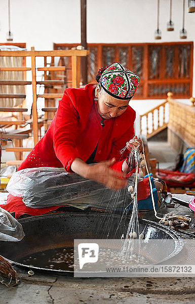 Uigurische Frau spinnt Seidenfaden aus Kokons in einer traditionellen Seidenwerkstatt  Jiya  Xinjiang  China  Asien
