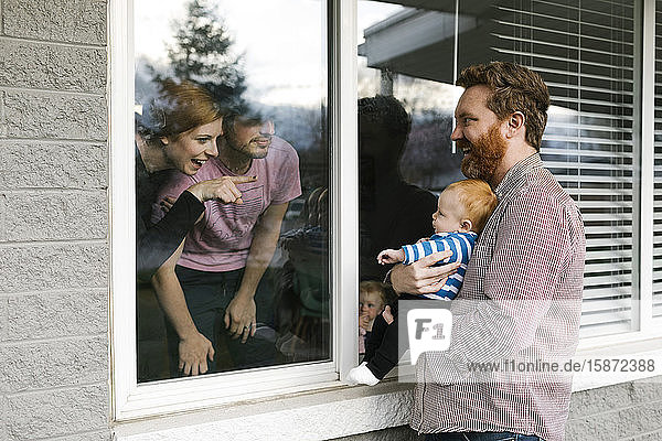 USA  Florida  Fort Myers Beach  Mann mit Babysohn (2-5 Monate)  der durch ein Fenster seine Familie besucht
