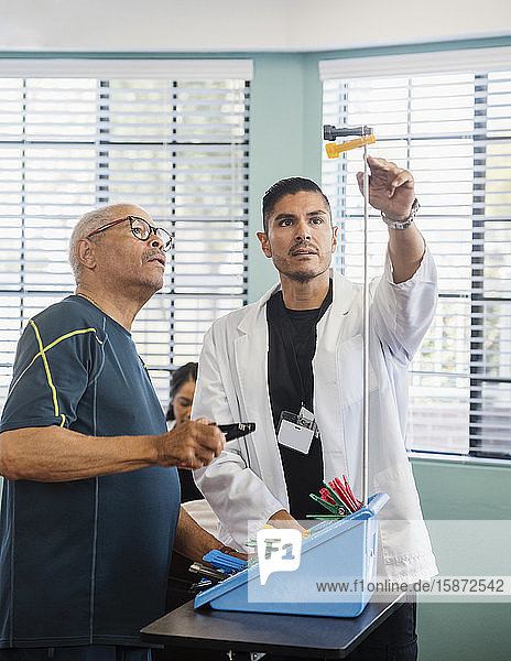 Arzt zeigt älterem Mann im Rehabilitationszentrum Pflöcke an der Stange