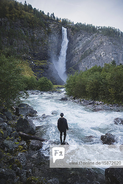 Junger Mann steht am Wasserfall