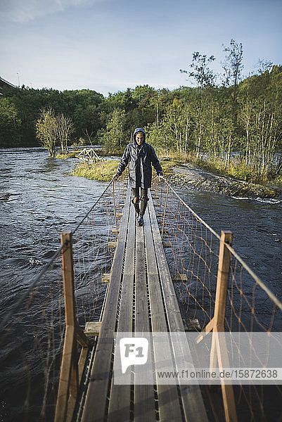 Junger Mann geht über eine Holzbrücke