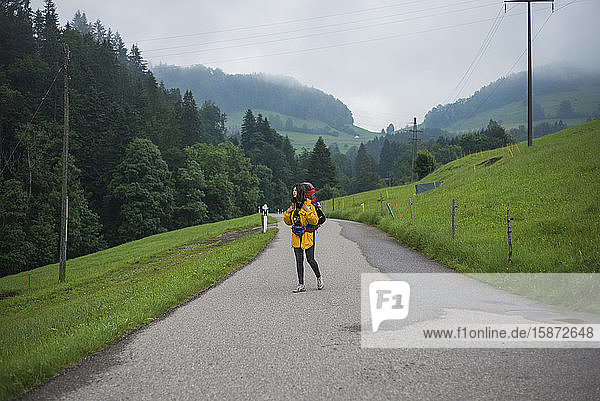 Young woman with yellow jacket and backpack walking along country road
