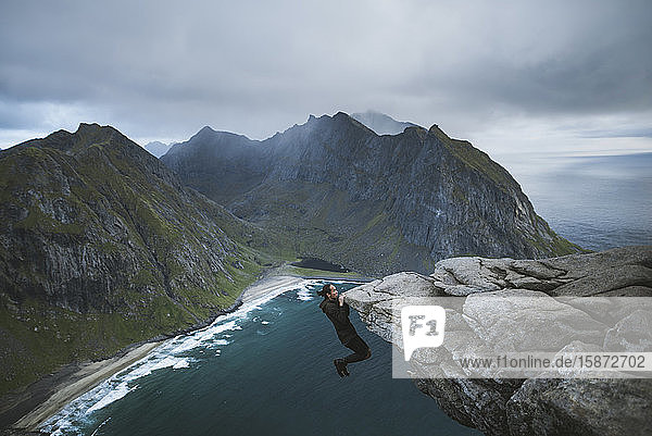 Mann hängt an einer Klippe auf dem Berg Ryten auf den Lofoten  Norwegen