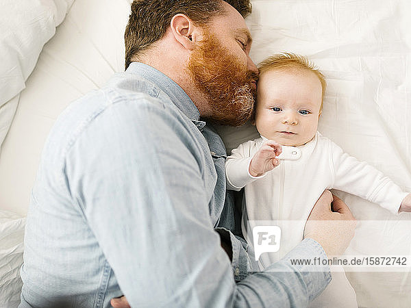 Father kissing baby boy (2-3 months) while lying on bed