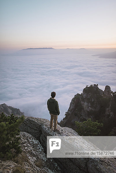 Junger Mann steht auf einem Berg über dem Nebel