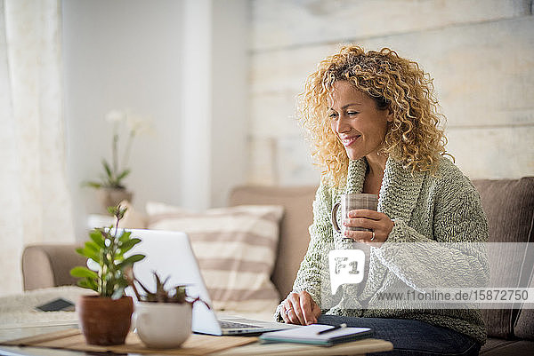 Smiling woman holding drink at laptop