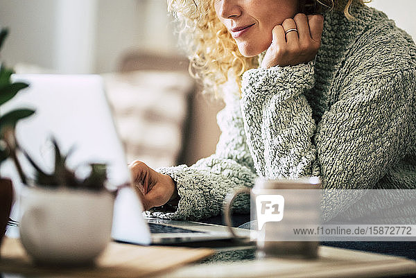 Lächelnde Frau arbeitet mit Laptop auf dem Sofa