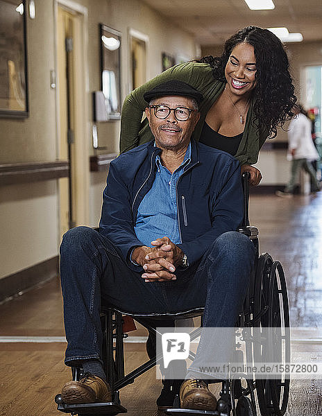 Lächelnde Frau  die einen älteren Mann im Rollstuhl schiebt