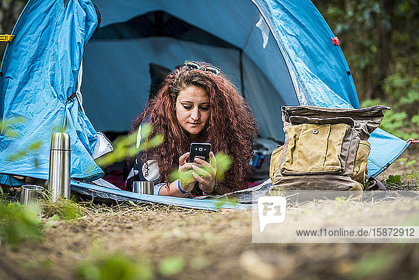 Woman lying in tent using smart phone