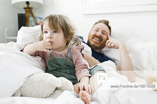 Tochter (2-3) und Vater sehen im Bett fern.
