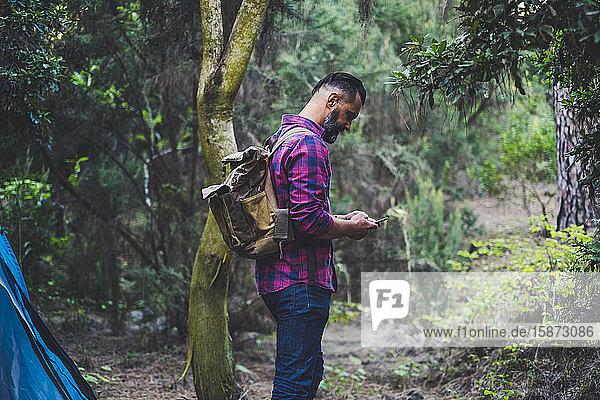 Mann mit Rucksack benutzt Smartphone im Wald