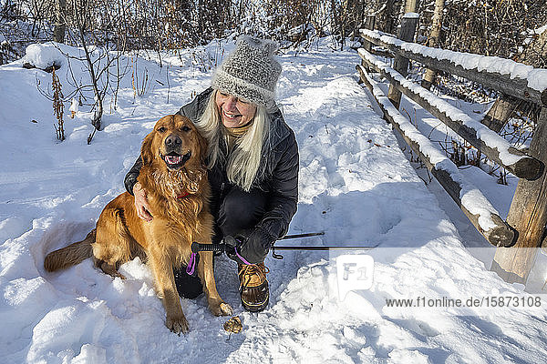 Smiling senior woman petting dog in snow