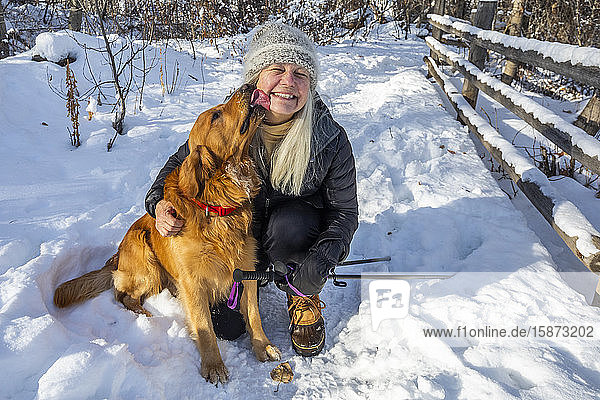 Lächelnde ältere Frau streichelt Hund im Schnee