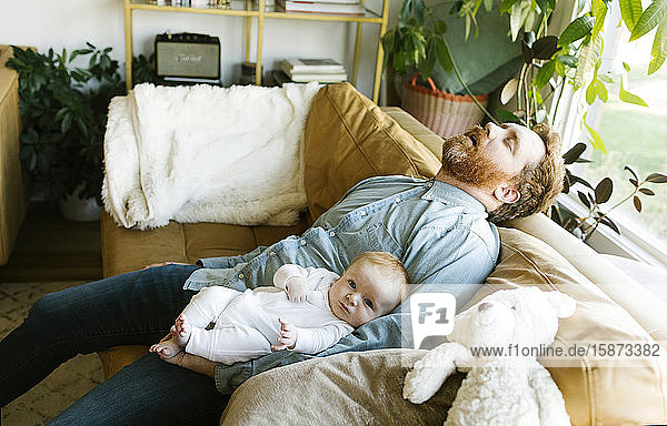 Schlafender Vater mit Babysohn (2-3 Monate) auf dem Sofa