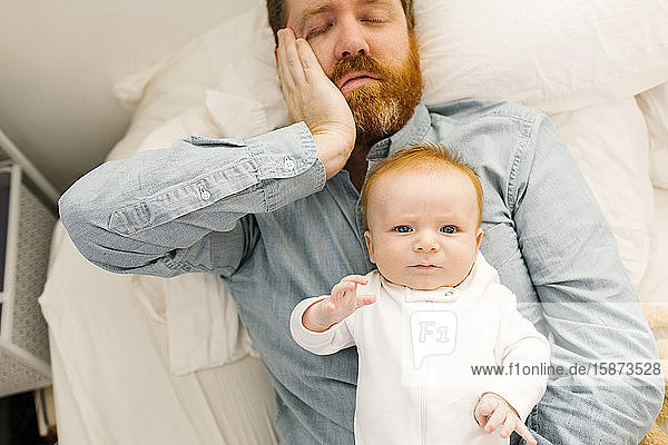 Vater liegt mit Baby im Bett (2-3 Monate)