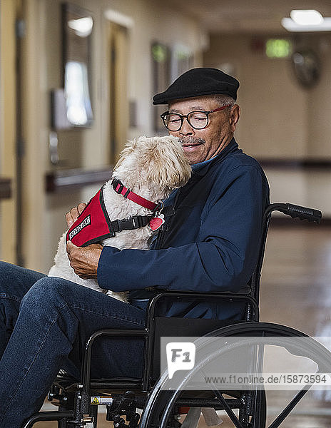 Älterer Mann hält Hund im Rollstuhl