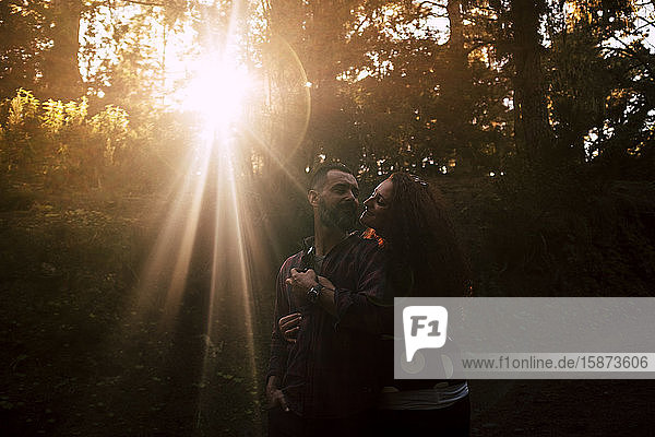 Lächelndes Paar  das sich im Sonnenlicht im Wald umarmt