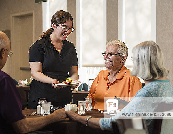 Smiling waitress handing food to smiling senior man