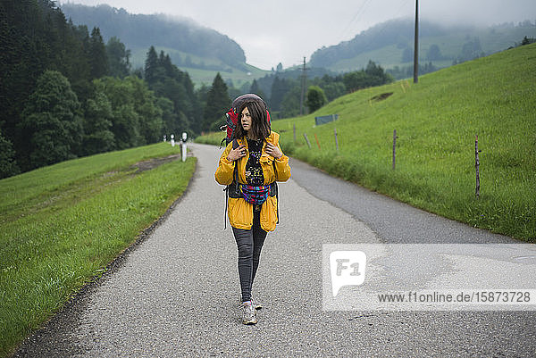 Junge Frau mit gelber Jacke und Rucksack auf der Landstraße